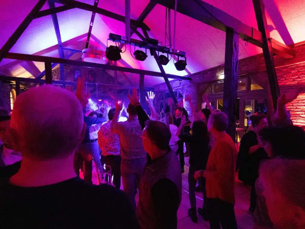 Ein voller Saal, die Hände in der Luft – hier wird getanzt, gefeiert und gelacht. Die stilvolle Beleuchtung in Lila- und Rottönen bringt Leben in die rustikale Architektur der Remise. Partystimmung pur.
